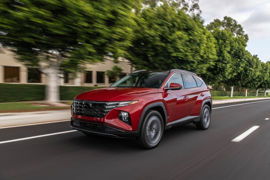 A red 2023 Hyundai Tucson SUV cruises down a road with green trees beside it. Hyundai has been cited as the year's best SUV brand.