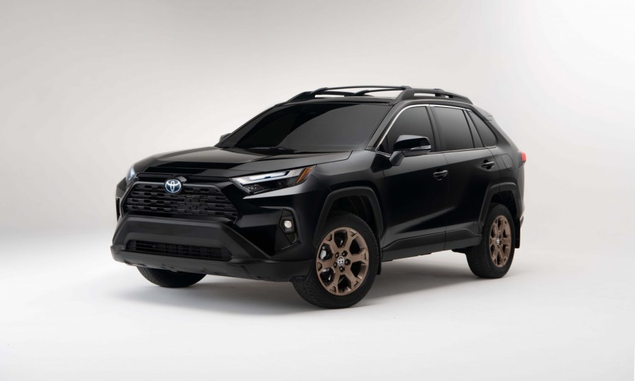 A black 2023 Toyota RAV4 Hybrid with gold wheels sits in a white room. 