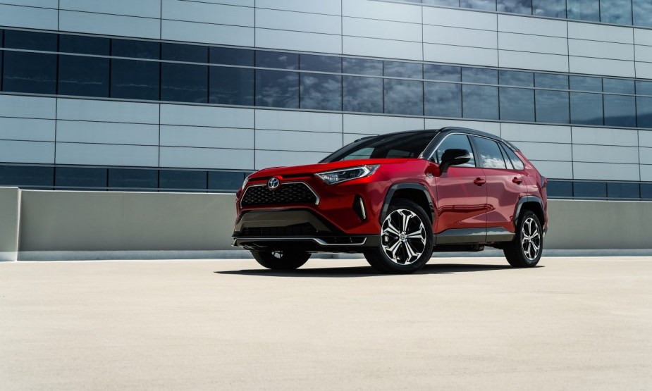 A red 2023 RAV4 Prime sits atop a parking garage near a large glass building. 