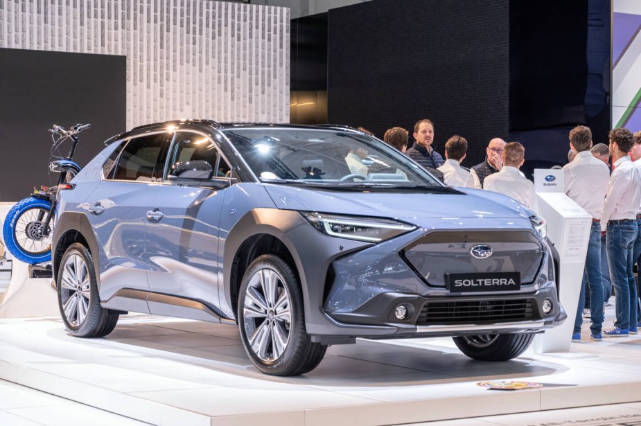 A blue 2023 Subaru Solterra EV SUV on display at an auto show with people around it. 