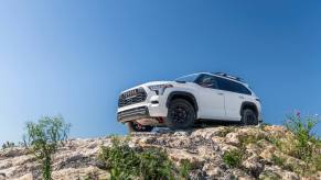 A white 2023 Sequoia drives on a rocky trail - view from below looking up with blue sky in background.