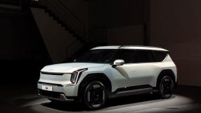 A white 2024 Kia EV9 full-size electric SUV model lit by a spotlight in a dark room