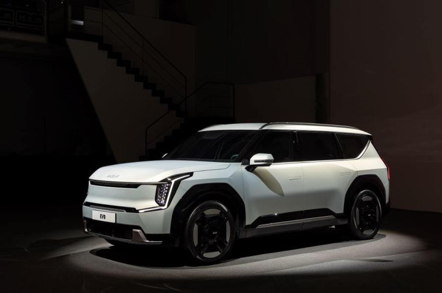 A white 2024 Kia EV9 full-size electric SUV model lit by a spotlight in a dark room