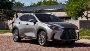 A silver Lexus RX sits on a pebble driveway in front of a home in midday sun.