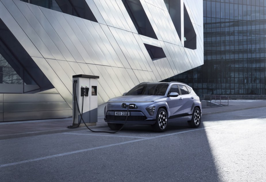 A new 2024 Hyunda Kona Electric plugged into a charging station in an urban landscape.