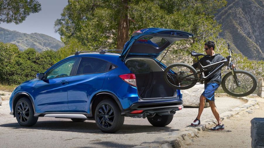 Man loading a mountain bike into the rear of a blue 2023 Honda HR-V subcompact SUV.