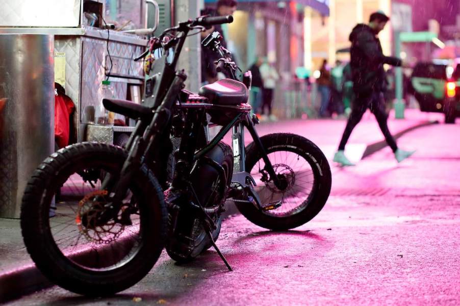 An E-bike parked outdoors on a a busy street.