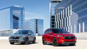 A blue Ford Escape PHEV sits to the left of a red Ford Escape ST-Line with a cityscape in the background.