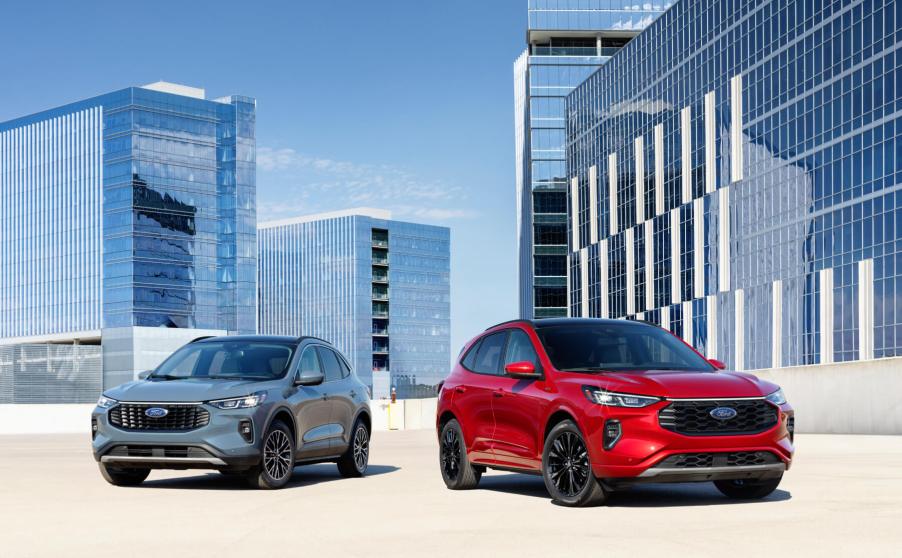 A blue Ford Escape PHEV sits to the left of a red Ford Escape ST-Line with a cityscape in the background.