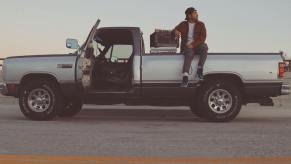 A man sits on the bed of his regular cab Dodge Ram pickup truck.