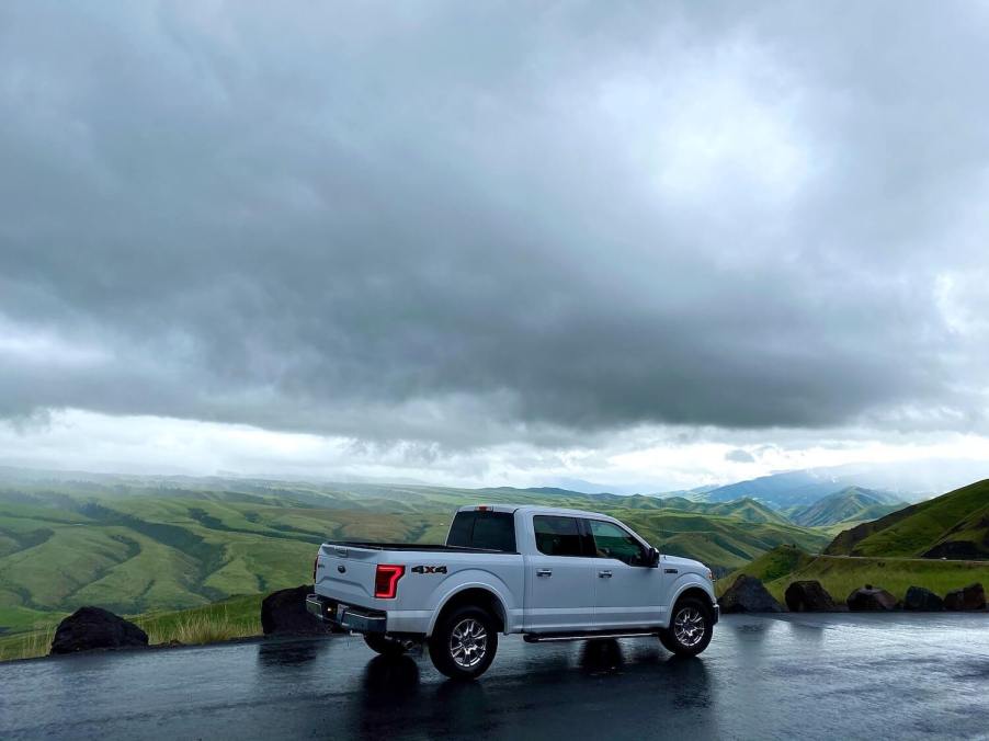 A white F-150 parked on a mountain road, a mountain range and dark clouds visible in the background.