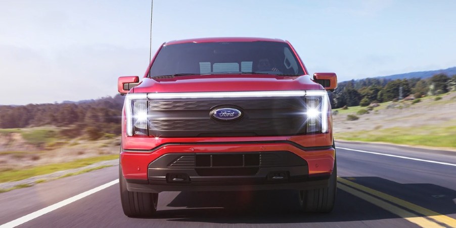 A red Ford F-150 Lightning electric pickup truck is driving on the road.