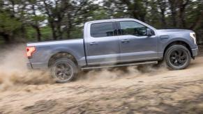 The side profile of a Ford F-150 Lightning Lartiat electric full-size pickup truck driving on a dusty road