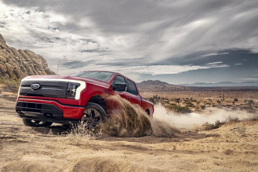 A red 2023 Ford F-150 Lightning drives through dirt as an electric truck.