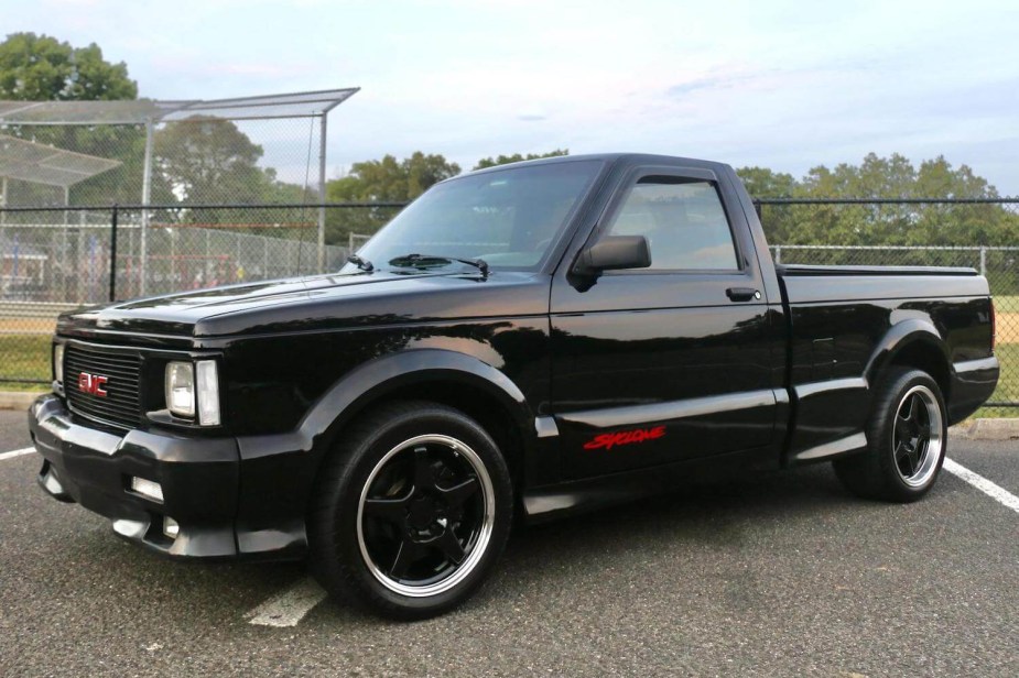 A black 1991 GMC Syclone supertruck parked in front of a fence for a promo shot.