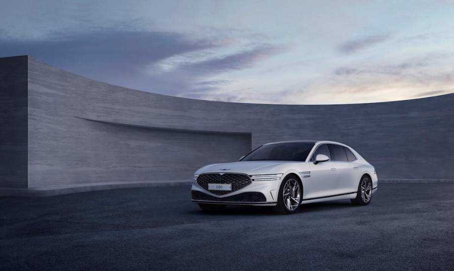 A white Genesis G90 parked in front of a grey building.