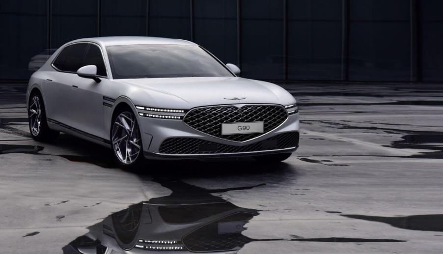 A silver-gray Genesis G90 luxury full-size sedan model parked on an asphalt floor splattered with water puddles