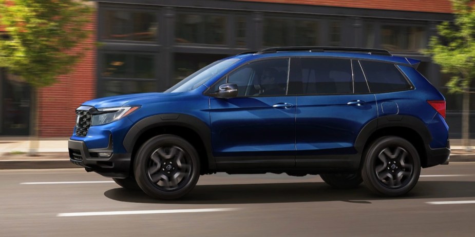 A blue 2023 Honda Passport midsize SUV is driving on the road. 