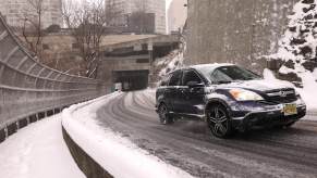 A Honda CR-V climbs a hill amid snowy conditions in an urban setting.