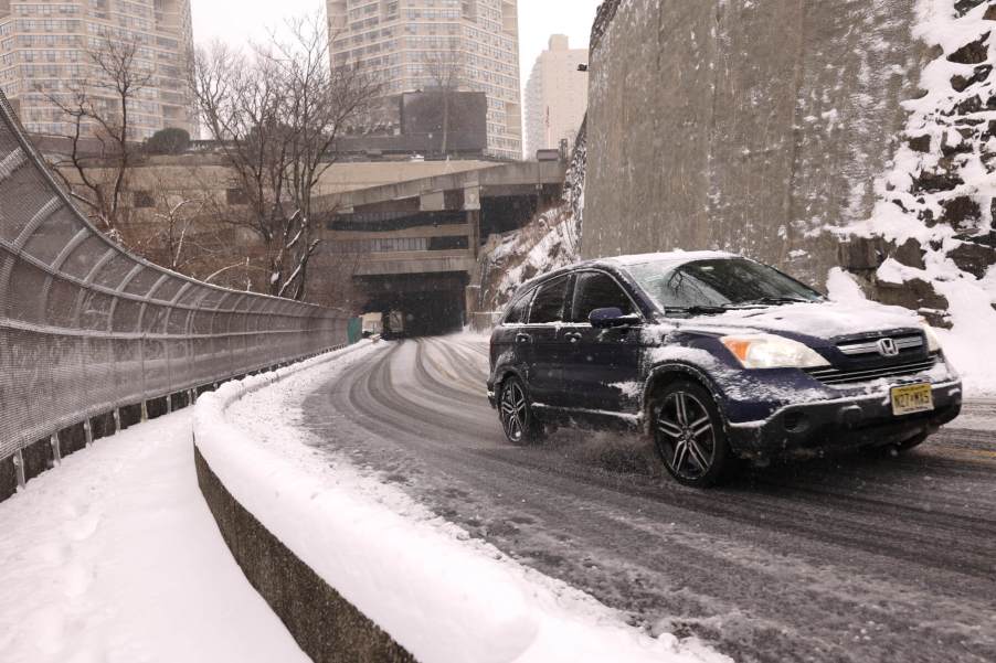 A Honda CR-V climbs a hill amid snowy conditions in an urban setting.