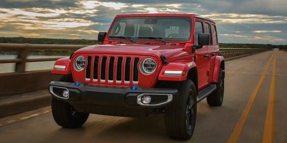 A red 2023 Jeep Wrangler small SUV is driving on the road. 