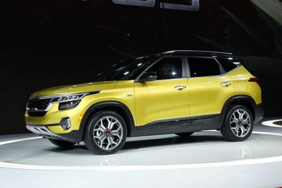 A yellow Kia Seltos parked indoors in front of a black background.