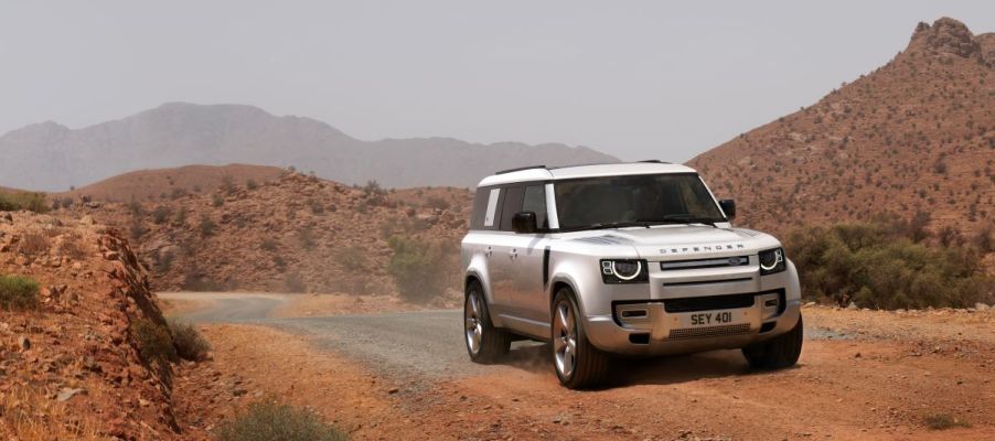 A white 2023 Land Rover Defender 130 drives near some mountains