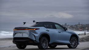 Rear view of a blue 2023 Lexus RZ 450e sitting on a beach underneath low clouds.