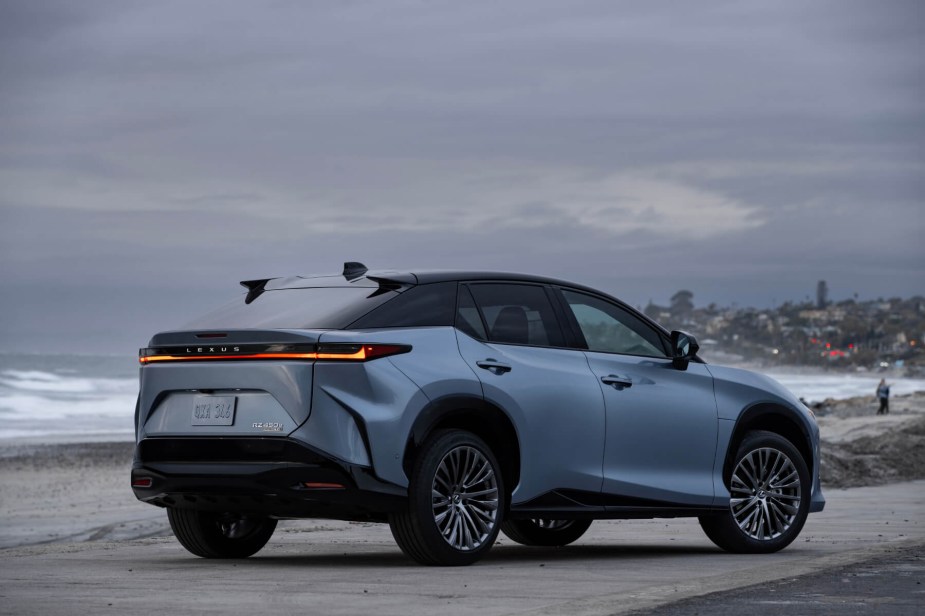 Rear view of a blue 2023 Lexus RZ 450e sitting on a beach underneath low clouds. 