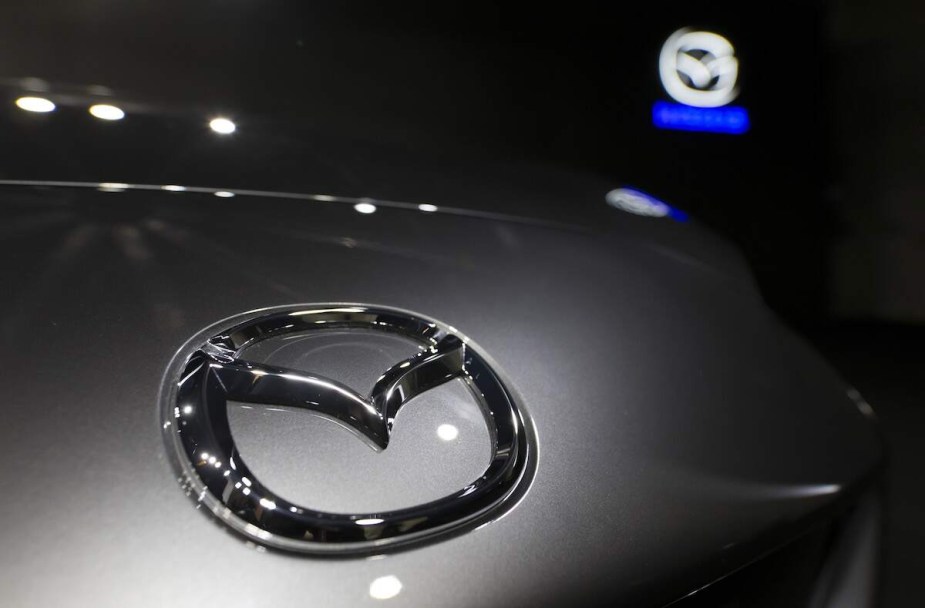 A Mazda logo on a Mazda MX-5, one of the top Mazda models, with a blurred Mazda logo in the background. 