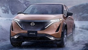 A copper 2023 Nissan Ariya small electric SUV is driving through the snow.