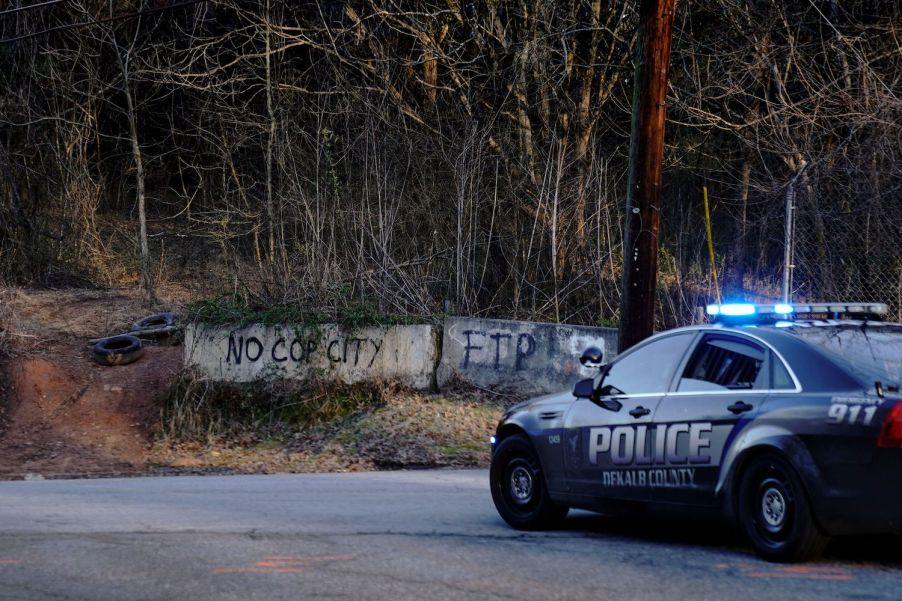 Police car stopped in front of a sign saying "No Cop City"