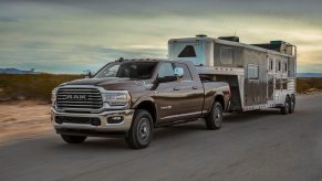 A RAm 2500 heavy duty pickup truck tows a livestock trailer down an empty road, the desert visible in the background.