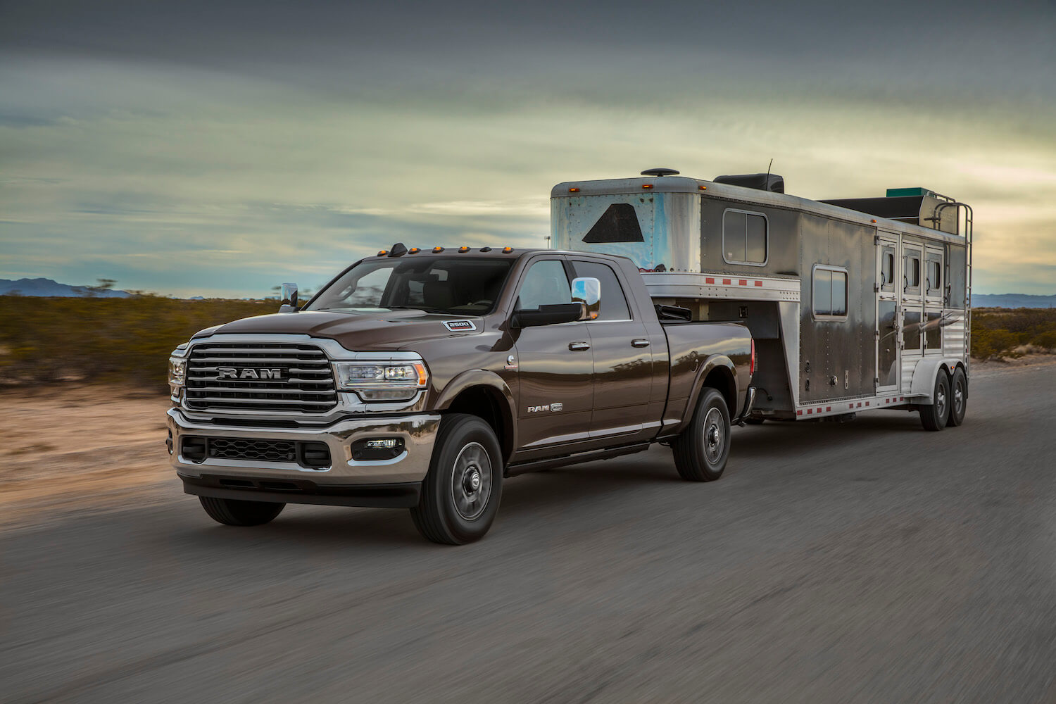 A RAm 2500 heavy duty pickup truck tows a livestock trailer down an empty road, the desert visible in the background.