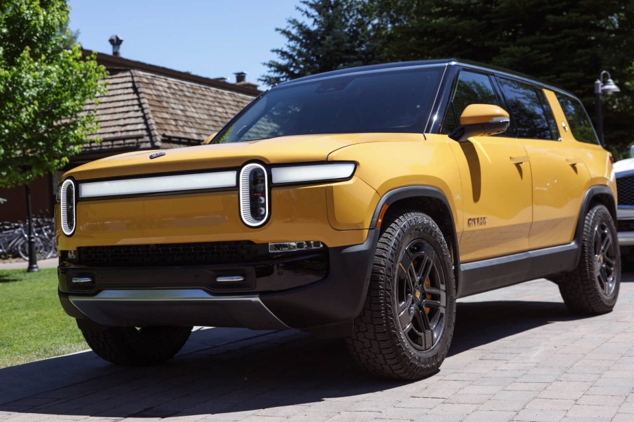 A yellow Rivian R1S electric SUV sits in front a green lawn under midday sun. 