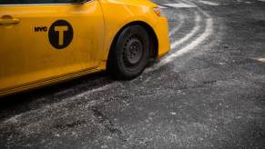 A yellow taxi drives on a street covered in road salt.