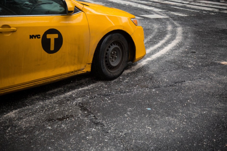 A yellow taxi drives on a street covered in road salt. 