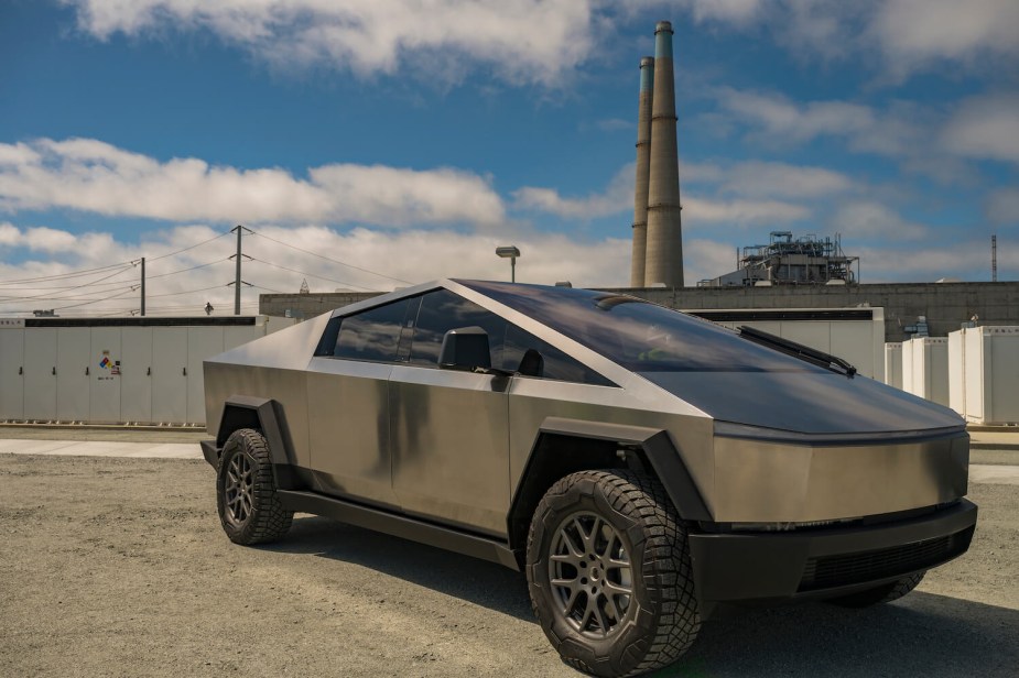 Photo of a Tesla Cybertruck prototype parked in front of a factory smokestak.