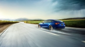 A blue Tesla Model 3 EV uses AWD to cut across a wet road.