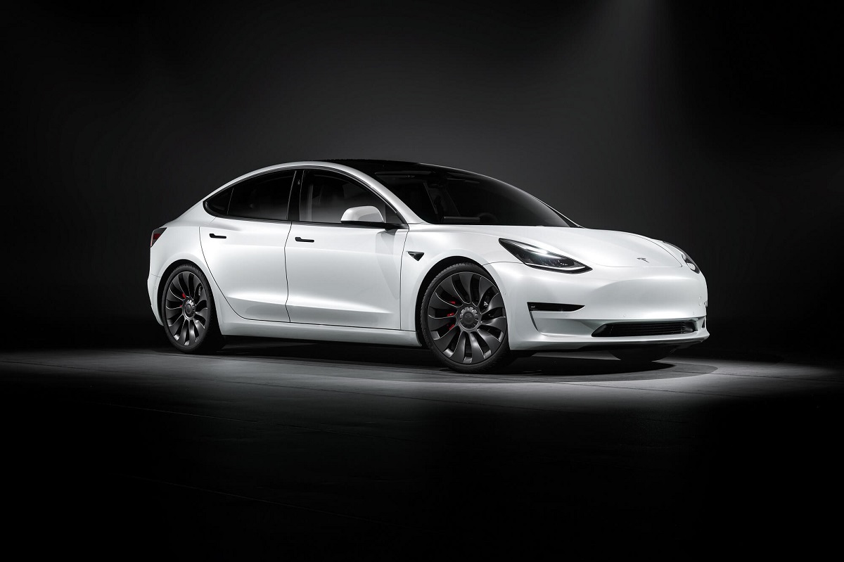 A white 2023 Tesla Model 3 poses in a dark studio.