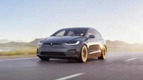 A gray 2023 Tesla Model X midsize SUV is driving on the road.