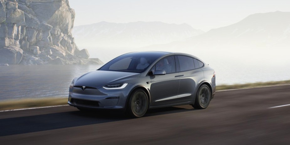 A gray 2023 Tesla Model Y small electric SUV is driving on the road. 