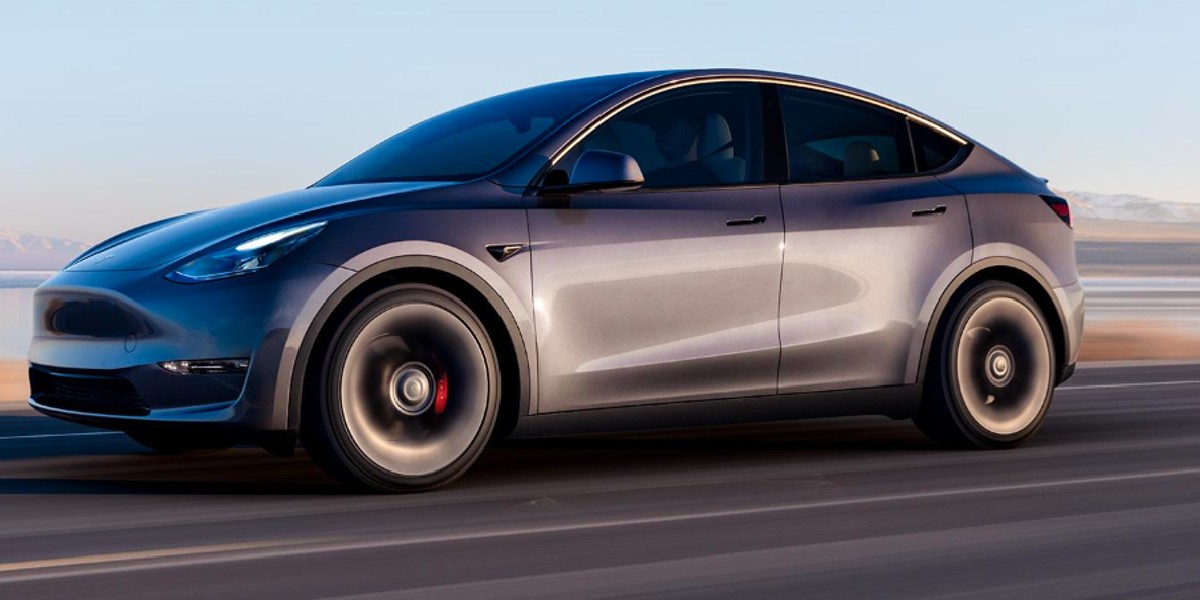 A gray 2023 Tesla Model Y small electric SUV is driving on the road.