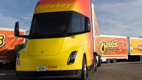 A yellow and red Tesla Semi truck operated by Frito Lay chip company, parked in front of a Cheeto trailer.