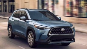 A blue 2023 Toyota Corolla Cross subcompact SUV is driving on the road.