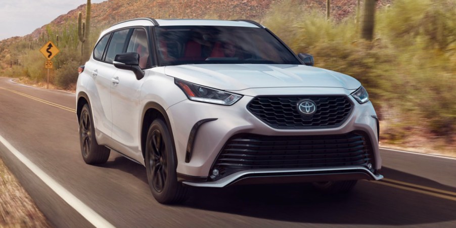 A white 2023 Toyota Highlander midsize SUV is driving on the road.