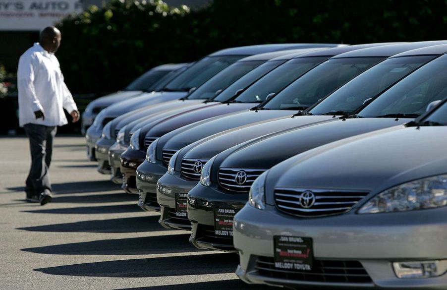 A man browses a row of used cars at a dealership.