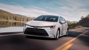 White 2023 Toyota Corolla compact sedan driving by a lake