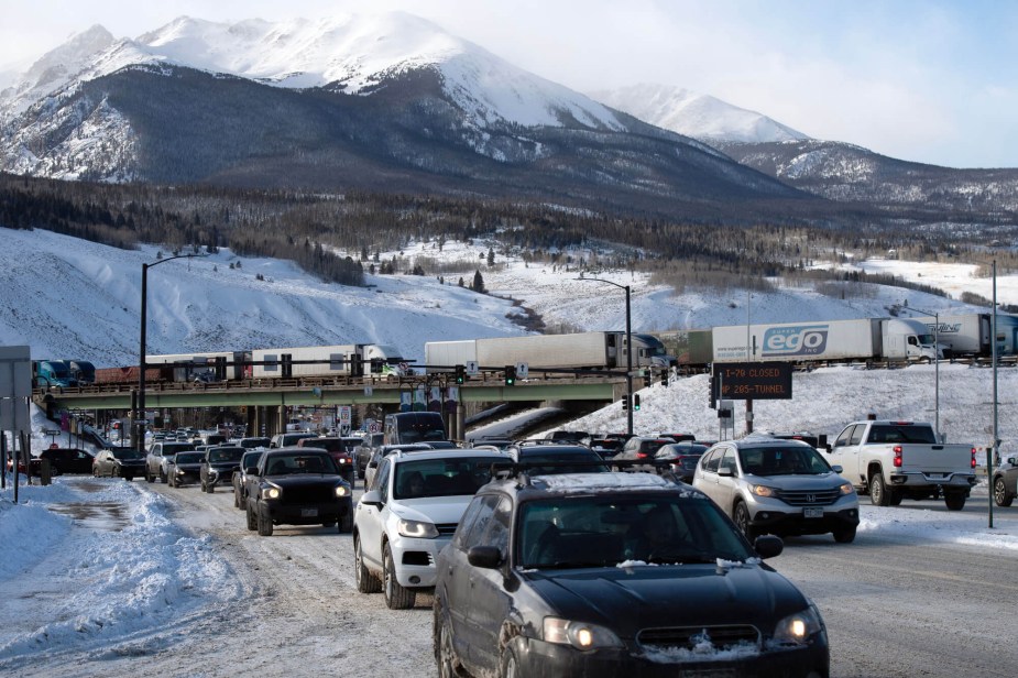 Cars drive on snowy roads with mountains in the background. 