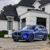 A blue 2023 BMW X7 full-size luxury SUV model parked on a cobblestone driveway outside a home